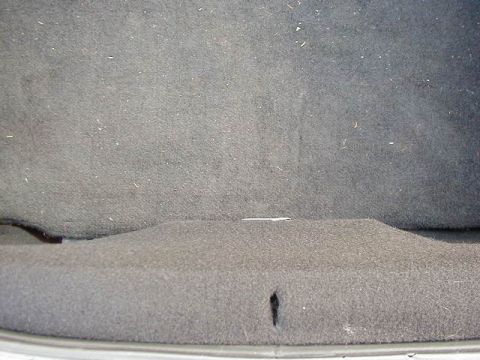1994 Ford Probe - The interior of a car's trunk is visible, covered in gray carpet with some dust and a small tear.