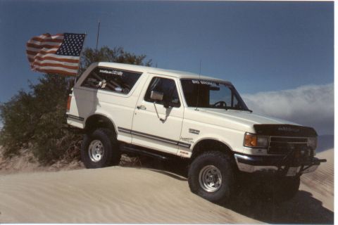 1990 Ford Bronco - White 1990 Ford Bronco with an American flag flying on a pole in a desert landscape.