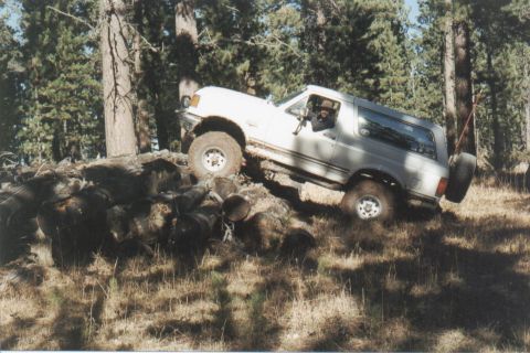 1990 Ford Bronco - This Ford Bronco is navigating a challenging off-road obstacle course in a forest setting.