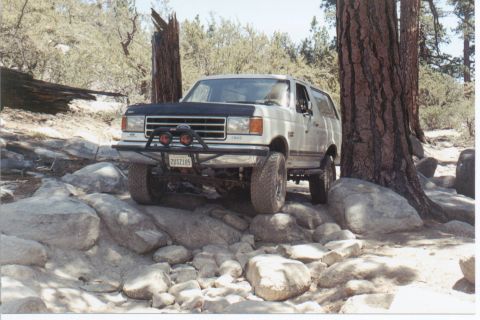 1990 Ford Bronco - White Ford Bronco navigates a challenging rocky trail, its front end angled towards the viewer.
