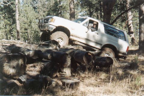 1990 Ford Bronco - White 1990 Ford Bronco navigates a difficult off-road obstacle of fallen logs.