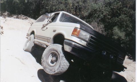 1990 Ford Bronco - This Ford Bronco is navigating a steep, rocky incline on an off-road trail.