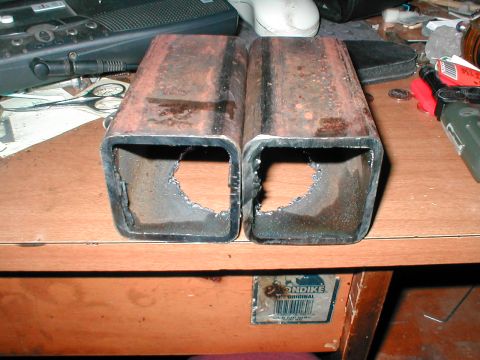 1979 Ford Bronco - Two rusty trailer hitch receivers with rough cutouts are shown on a wooden surface, with various tools and electronic equipment in the back…