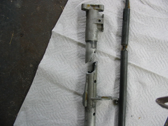 Broken metal rod and housing on a white paper towel. Text overlay reads SUPERMOTORS.NET