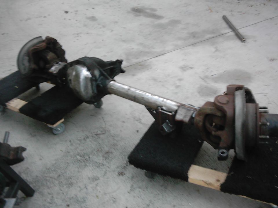 Rear axle assembly on wooden blocks with casters, showing differential housing, driveshaft U-joint, and brake components