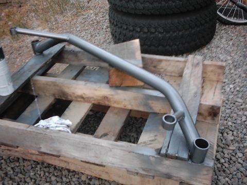 1978 Ford Bronco - A painted metal part rests on a wooden pallet, with stacked tires visible behind it.
