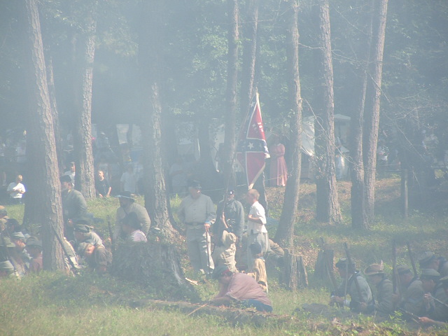 Civil War reenactment with soldiers and a Confederate flag in a wooded area