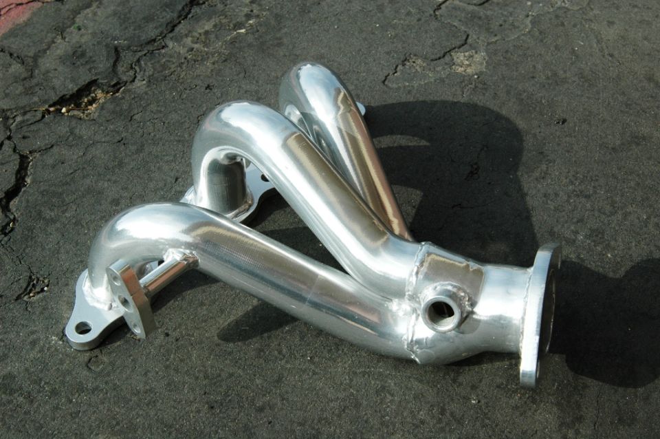 Polished 3-into-1 exhaust header with O2 sensor bung lying on cracked asphalt