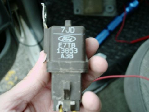 1988 Ford Bronco - A hand holds a dusty brown Ford relay stamped '7JD' and part number E7TB-13853-A3B above its blue Ford oval, with the spade terminals and m…