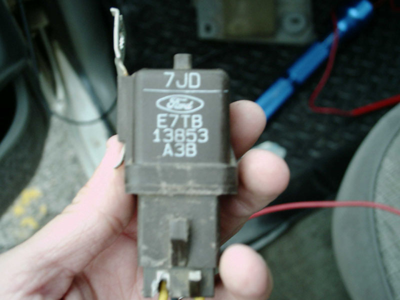 Hand holding brown Ford relay stamped E7TB-13853-A3B with blue Ford oval logo