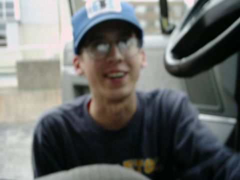 1988 Ford Bronco - Blurry candid of a young man in a light blue ball cap, wire-rim glasses and navy sweatshirt sitting in the passenger seat, shot from the dr…