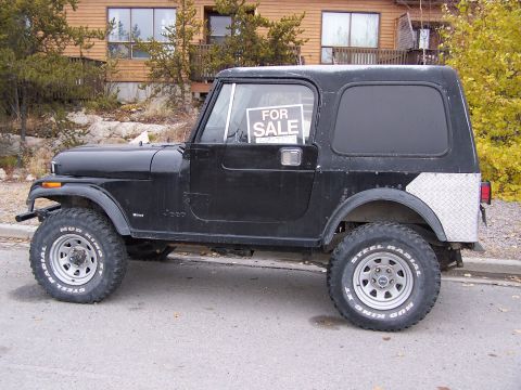 1983 Jeep CJ7 - A black 1983 Jeep CJ7 is parked on a street with a house in the background.