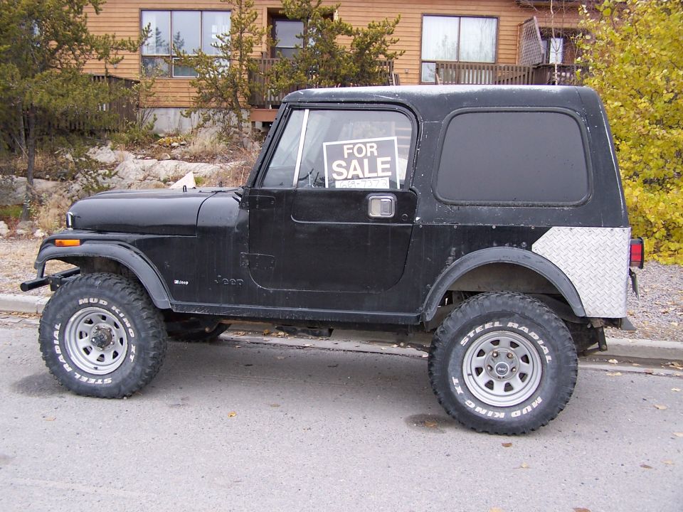 Black lifted Jeep CJ7 hardtop in side view with For Sale sign in window, parked on street.