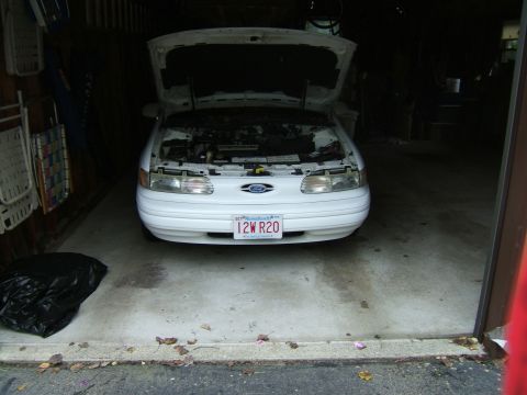 1998 Ford Taurus - A white 1998 Ford Taurus is parked in a garage with its hood open, revealing the engine.