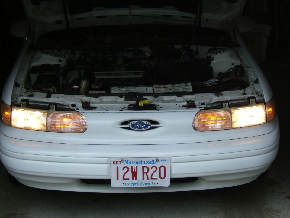 Front view of a white 1998 Ford Taurus with hood open, showing the engine. Massachusetts license plate 12W R20