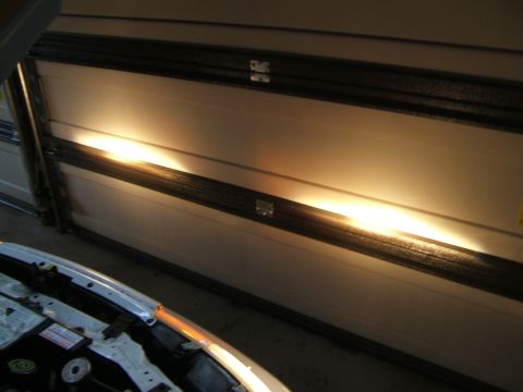 1998 Ford Taurus - Headlights shine on a garage door with the car's hood open.