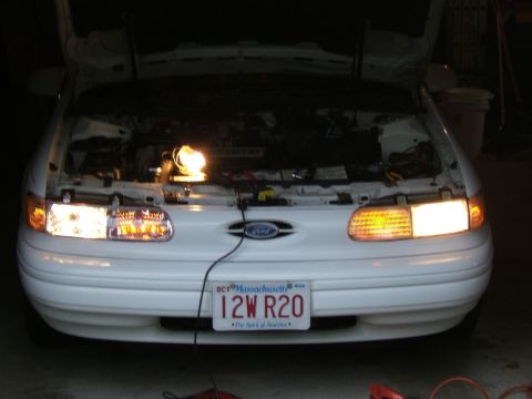 1998 Ford Taurus - Front view of a 1998 Ford Taurus with its hood open, showing the engine bay illuminated by a work light.