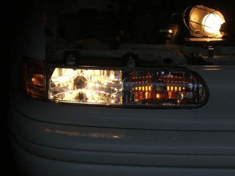 1998 Ford Taurus - Close-up of illuminated car headlights and turn signals with the hood open and a work light providing illumination.