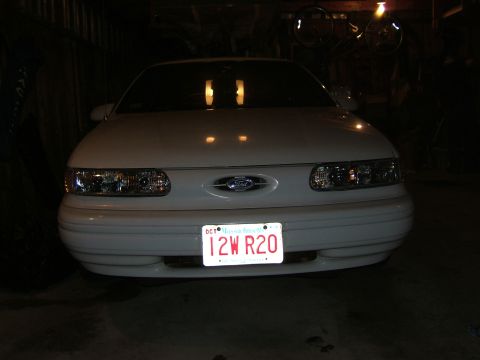 1998 Ford Taurus - A white 1998 Ford Taurus is parked indoors, facing the camera with its headlights illuminated.
