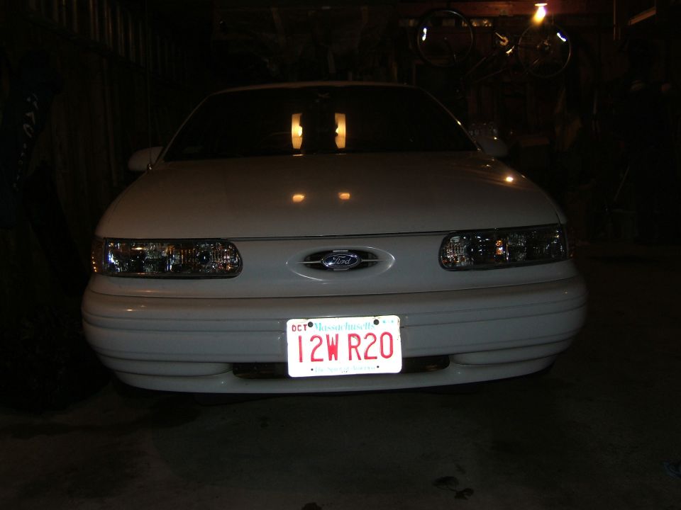 Front view of a white 1998 Ford Taurus with its headlights on