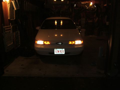 1998 Ford Taurus - A 1998 Ford Taurus is parked in a garage with its headlights illuminated.