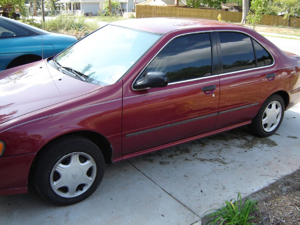 Maroon Nissan Sentra sedan with tinted windows and hubcaps parked on a driveway