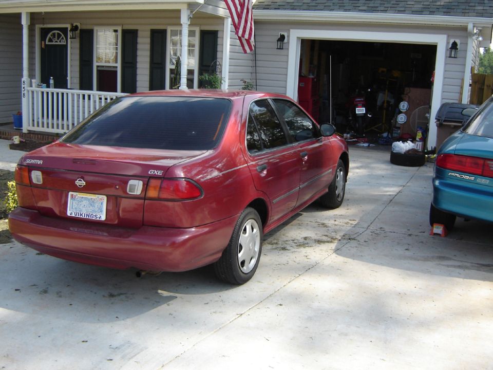 Dark red Nissan Sentra GXE sedan with tinted windows, three-quarter rear view on driveway