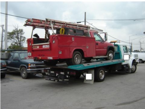1992 Ford Bronco - A red service truck is being transported on a flatbed tow truck, with another vehicle parked nearby.