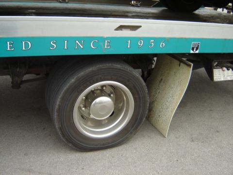 1992 Ford Bronco - A tow truck's side is visible, a teal stripe with text and a large tire.