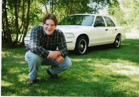 2000 Ford Crown Victoria - A white 2000 Ford Crown Victoria is seen from a 3/4 front angle, parked on grass with a person crouching in front of it.