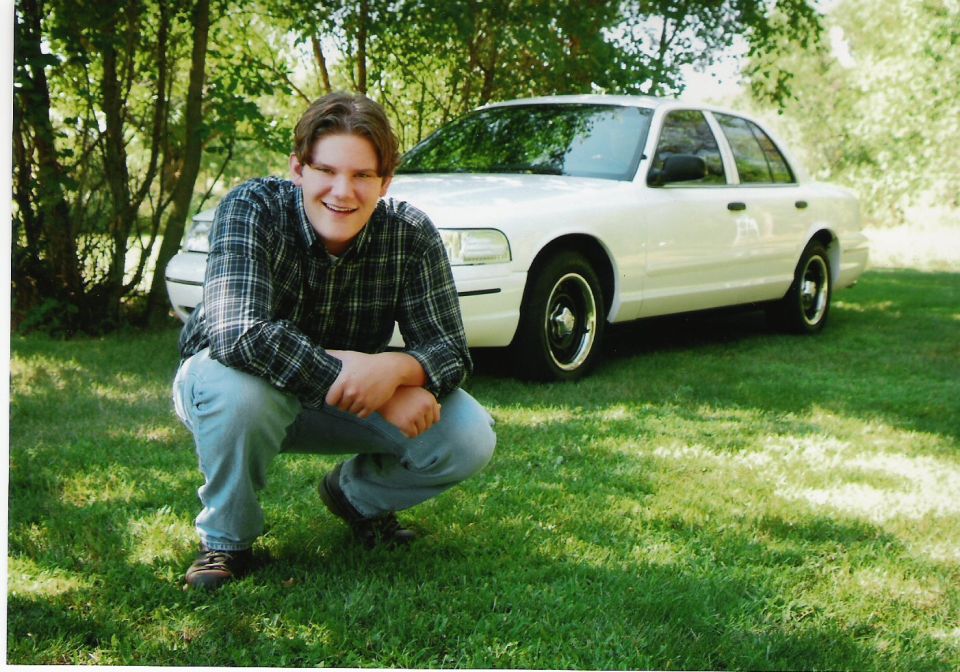 White 2000 Ford Crown Victoria 3/4 front view with a person crouching in front