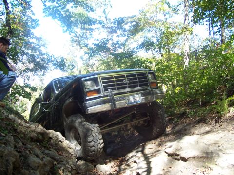 1986 Ford Bronco - A black Ford Bronco tackles a challenging off-road trail with a person watching from the side.