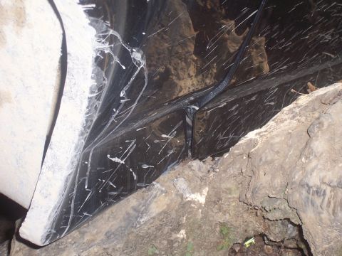 1986 Ford Bronco - The underside of a black vehicle is covered in white paint splatters and dirt, with rocks visible around it.