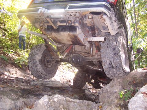 1986 Ford Bronco - An off-road vehicle navigates a challenging rocky path, showing its undercarriage and large tires.