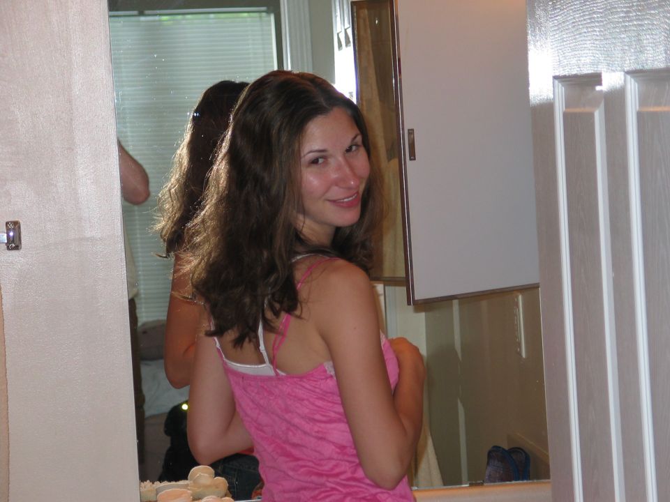 Smiling woman with long brown hair in a pink top looking over her shoulder