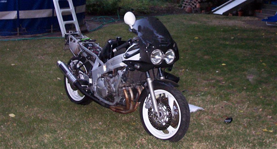 Black Yamaha FZR600 with tail bodywork removed, exposed frame and engine, twin headlights, white wheels, park…