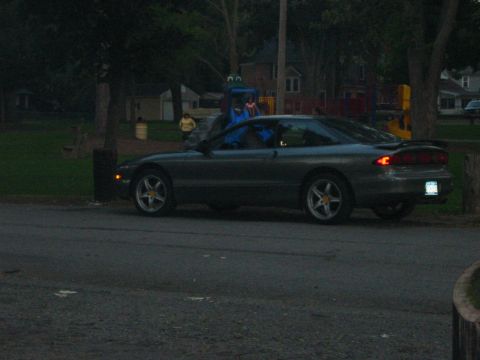 1996 Ford Probe - A dark gray coupe is parked on the side of the road near a park.