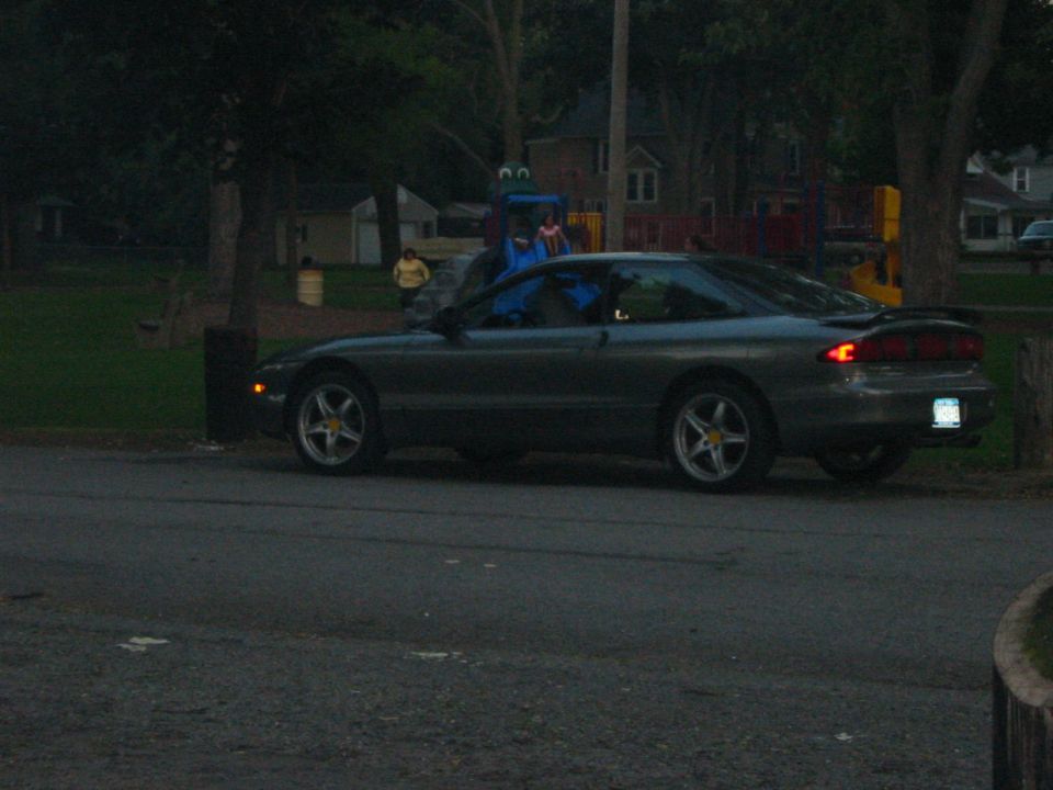 Dark gray coupe parked on asphalt, side view. Visible spoiler and alloy wheels