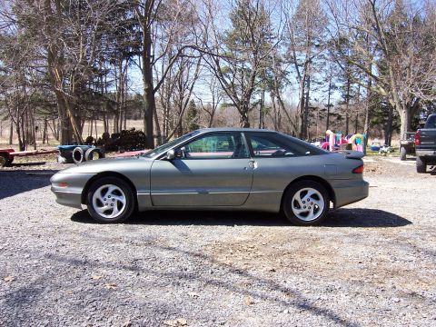 1996 Ford Probe - A gray Ford Probe coupe is parked on a gravel lot with trees in the background.