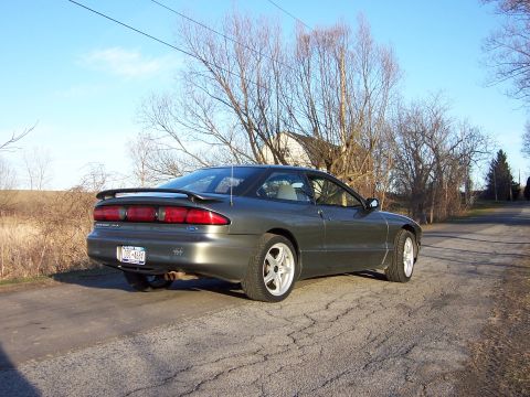 1996 Ford Probe - A dark gray 1996 Ford Probe is parked on a cracked asphalt road, with bare trees and a house in the background.