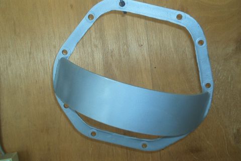 1983 Ford Bronco - A differential cover gasket and a curved metal shield are shown against a wooden background.