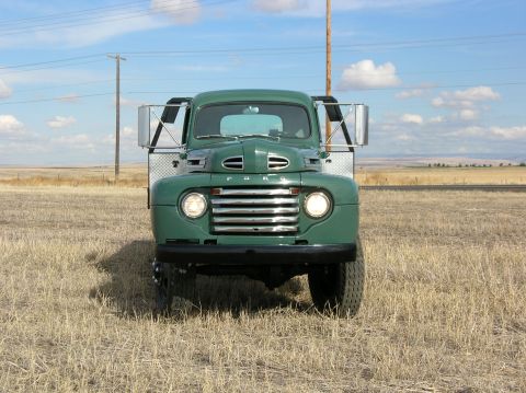 1949 Ford F5 - A green 1948 Ford truck is seen from the front, parked in a grassy field under a partly cloudy sky.