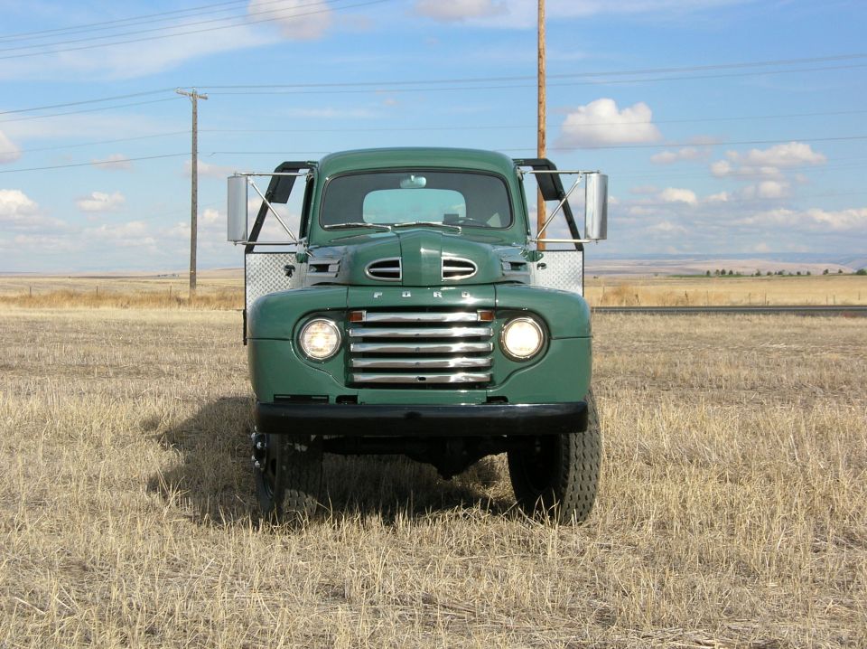 Green vintage Ford truck front view in a dry grassy field under blue sky