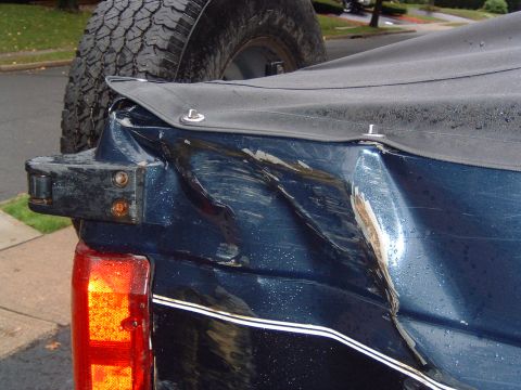 1993 Ford Bronco - The rear of a dark blue SUV shows extensive damage to the body panel, with a spare tire visible above.