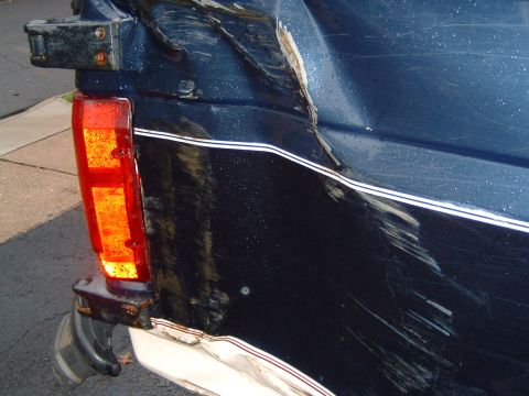 1993 Ford Bronco - The rear of a damaged dark blue SUV, with a broken taillight and extensive body damage visible.