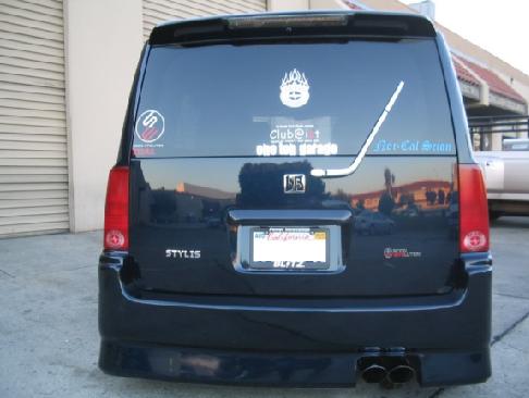 Rear of black minivan with Stylis badge and many window stickers in parking lot