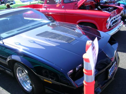 1996 Ford Probe - A dark blue car with flame decals on its hood is parked next to a red pickup truck at a car show.