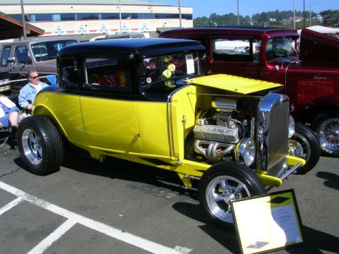 1996 Ford Probe - A custom hot rod with a two-tone yellow and black paint scheme and a prominent V8 engine is displayed at a car show.