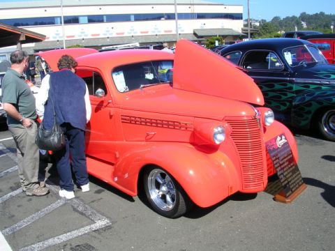 1996 Ford Probe - A bright red vintage car is displayed with its hood open at a car show, with another customized car visible behind it.
