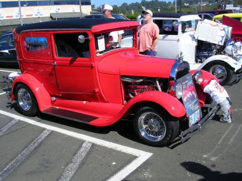 1996 Ford Probe - A red sedan hot rod with a black top is parked at a car show. A child looks at a sign on the front.